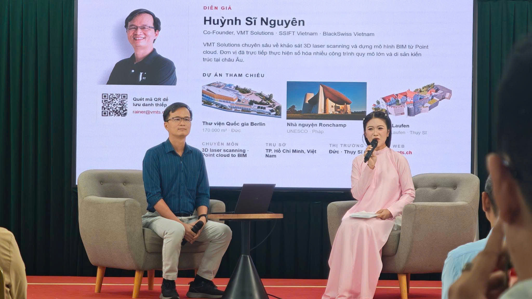 Huỳnh Sĩ Nguyên, Co-Founder VMT Solutions, cùng MC trên sân khấu, slide giới thiệu diễn giả và 3 dự án tham chiếu Thư viện Quốc gia Berlin, Ronchamp, Laufen